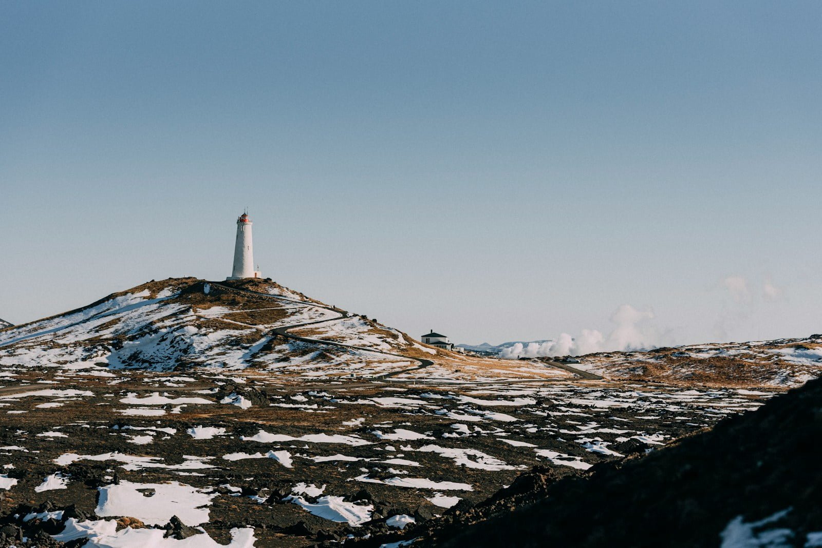 A mountain with snow on the ground and a light house in the distance