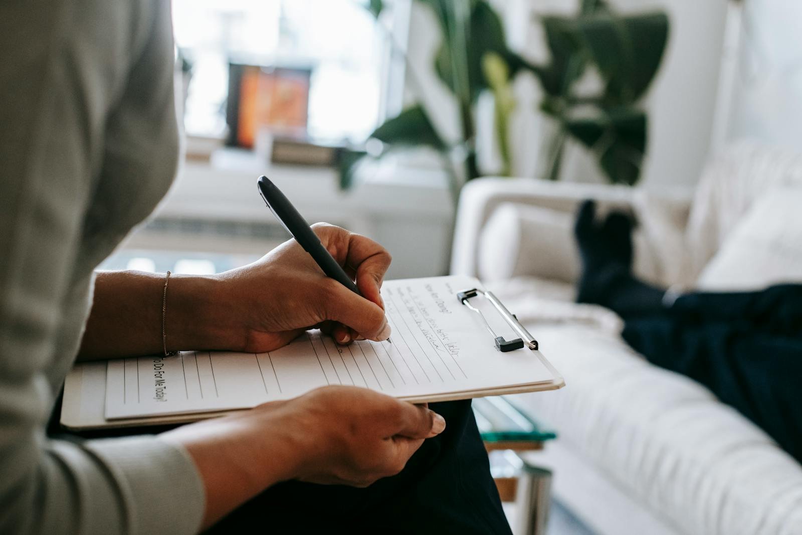 emale therapist taking notes on clipboard while filling out form during psychological appointment with anonymous client lying on blurred background